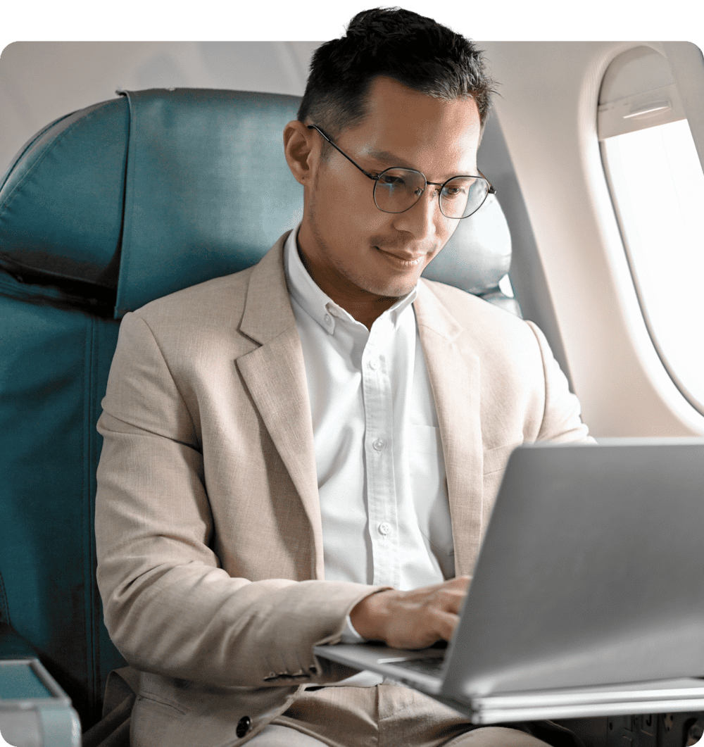 A man sit on a seat of an airplane, working with is laptop